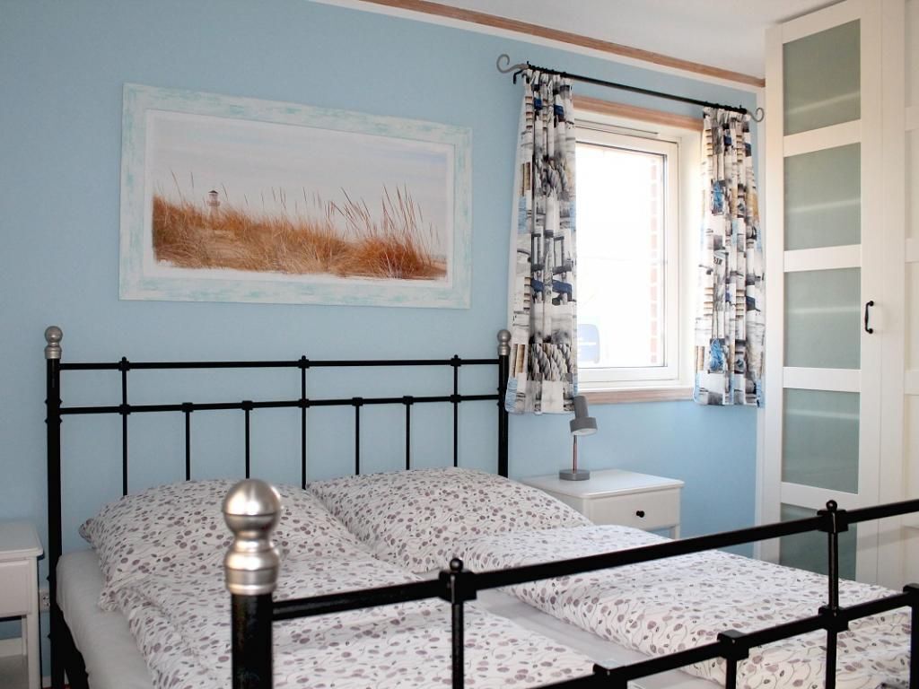 A bedroom with a bed, a nightstand, a lamp, a window with patterned curtains, and a door with frosted glass panels.
