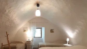 A cozy attic bedroom with a sloped ceiling, a large bed, two bedside tables, a chair, and a window with curtains.