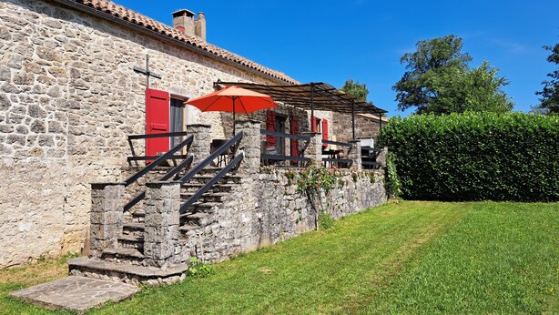 A stone building with a tiled roof, a staircase leading to a porch, and a red umbrella.