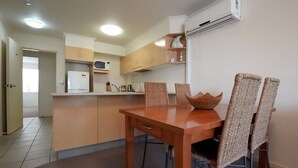 Uma cozinha compacta com área de jantar, apresentando uma mesa de madeira e cadeiras de vime, micro-ondas e ar condicionado instalado.