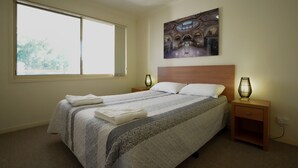Quarto com uma cama grande, duas luminárias de cabeceira, um quadro na parede e uma janela com cortinas.