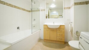 Um banheiro moderno com chuveiro em cabine de vidro, pia branca, armários de madeira e vaso sanitário.