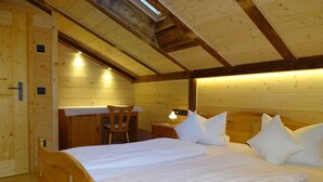 Ein Schlafzimmer einer Holzhütte mit einem Bett, einem Sessel, einem Nachttisch und einem Schreibtisch.