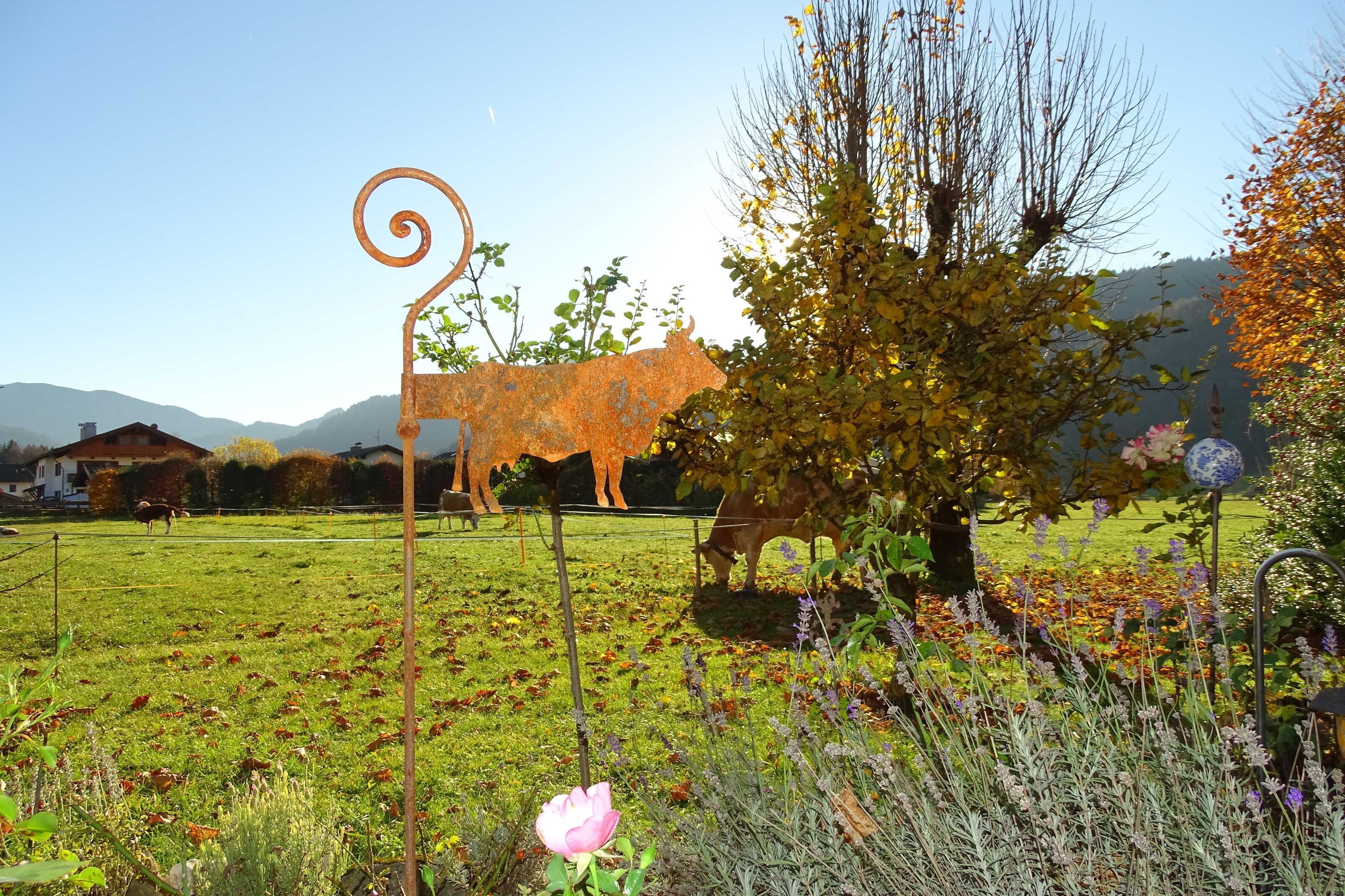 A rural landscape with a metal sculpture of a cow, a tree, and a field.