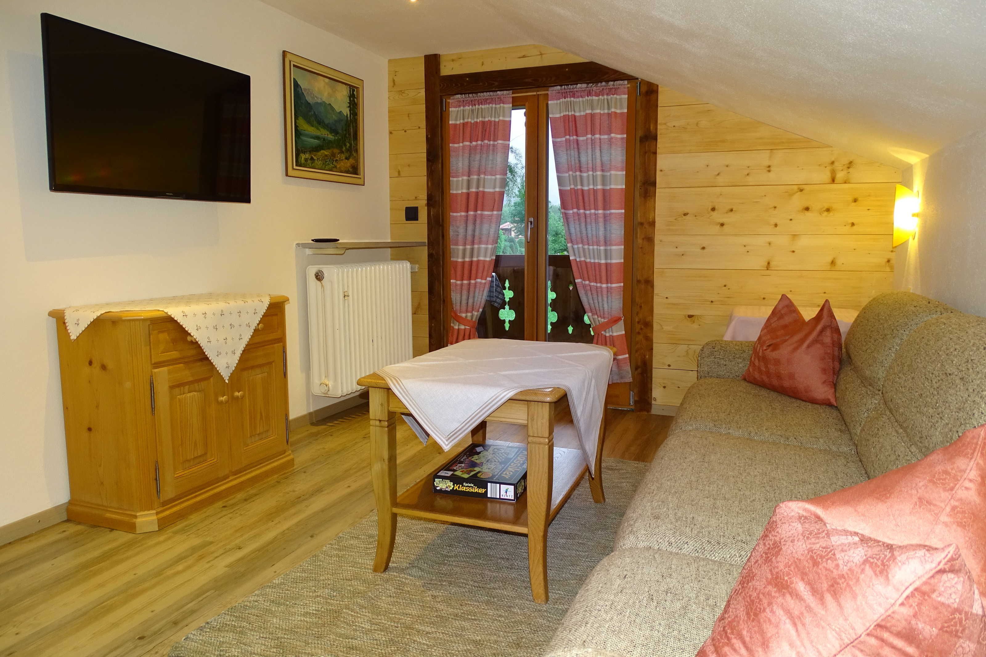 Een gezellige kamer met een houten plafond, een bank, een tafel en een radiator.