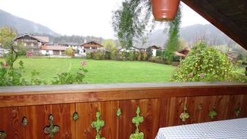 A wooden deck with a table and chairs, a view of a green lawn, and houses in the background.