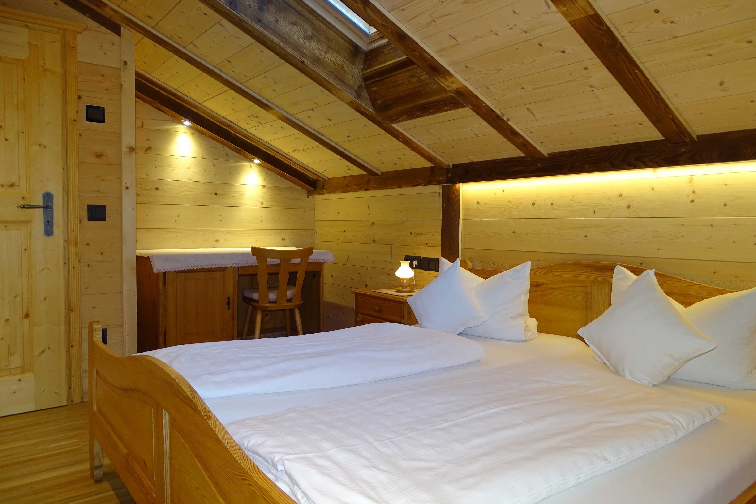 Een slaapkamer in een houten chalet met een bed, een stoel, een nachtkastje en een bureau.