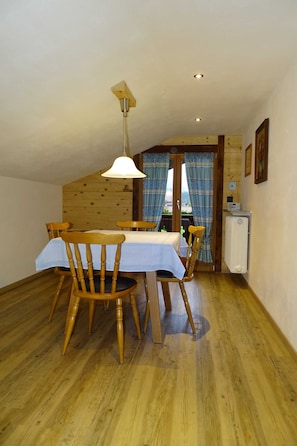 Un coin repas avec des chaises en bois, une table recouverte d’une nappe blanche, un luminaire suspendu et un radiateur fixé au mur.