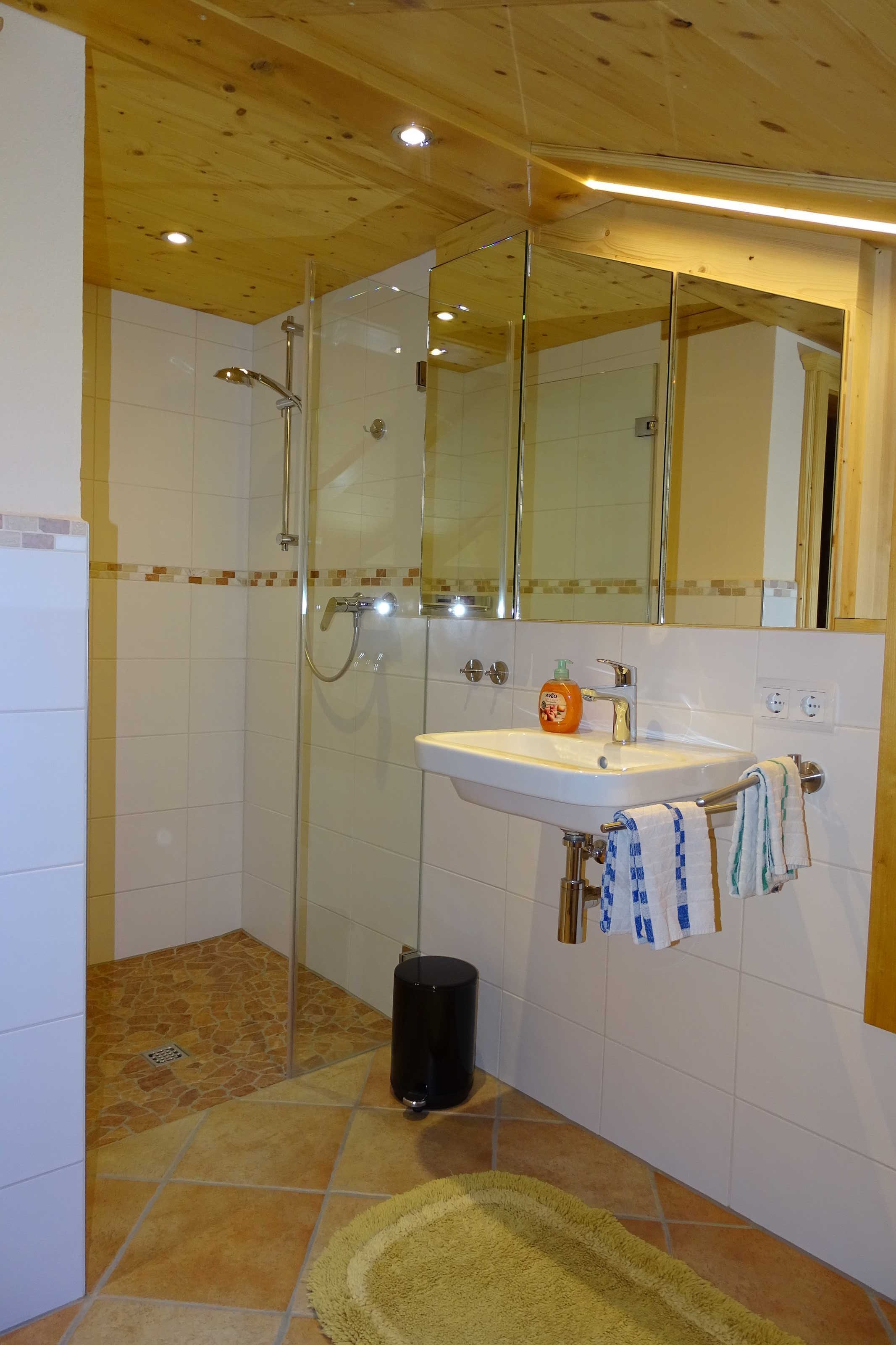 Een badkamer met een douchecabine van glas, een wastafel met spiegel erboven en een betegelde vloer.