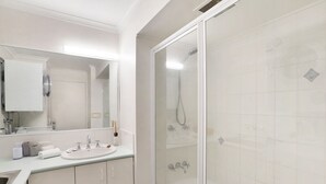 Moderni kylpyhuone, jossa on lasiseinällä varustettu suihku, peilillä varustettu pesuallas ja vasemmalla puolella näkyvissä oleva wc-istuin.
