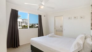 Hotellihuone, jossa on sänky, kattotuuletin, ikkuna verhoilla ja näkymä ulkopuolella oleviin rakennuksiin.