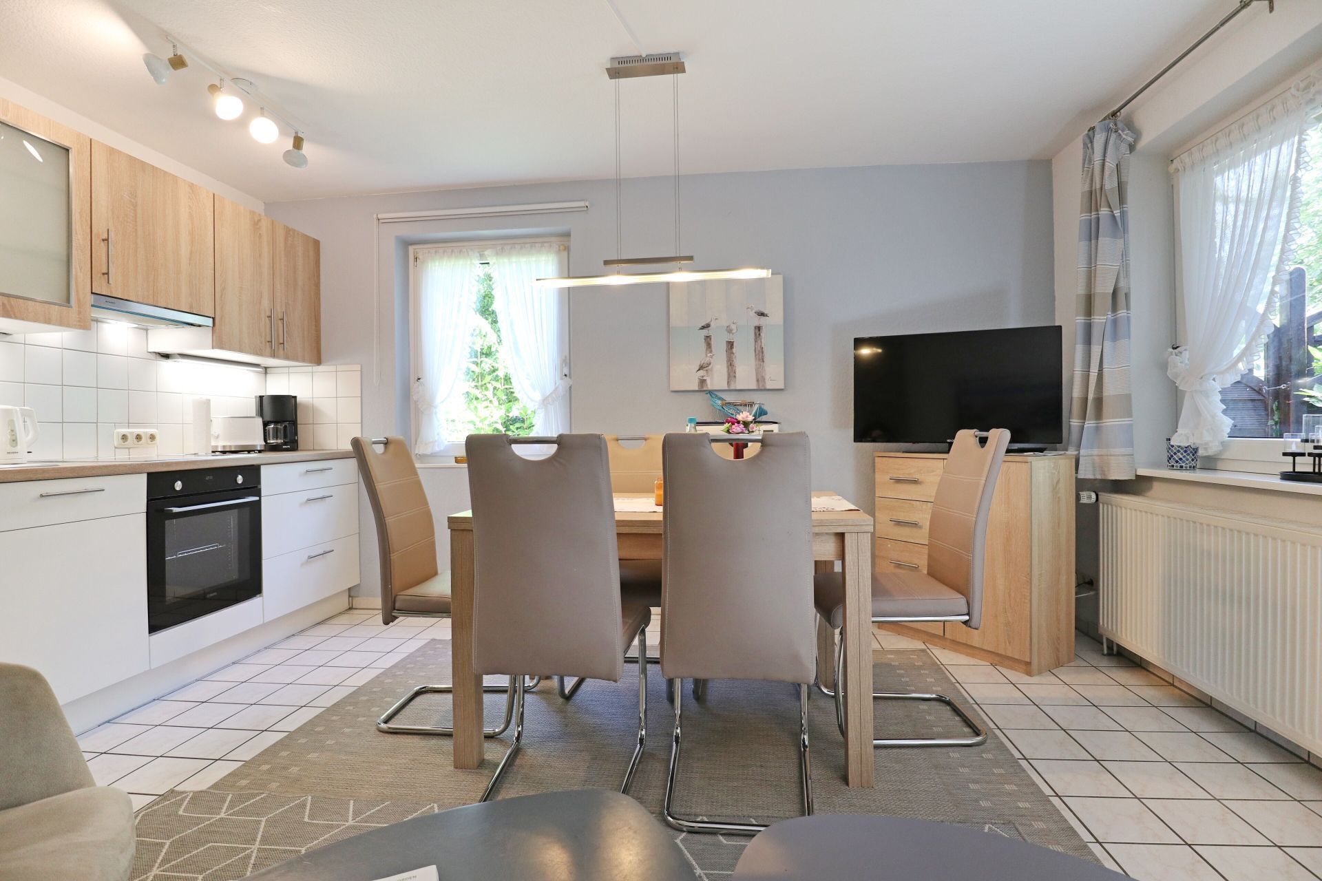 Una cocina moderna con comedor, televisor y ventana con cortinas.