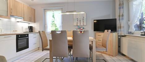 Una cocina moderna con comedor, televisor y ventana con cortinas.