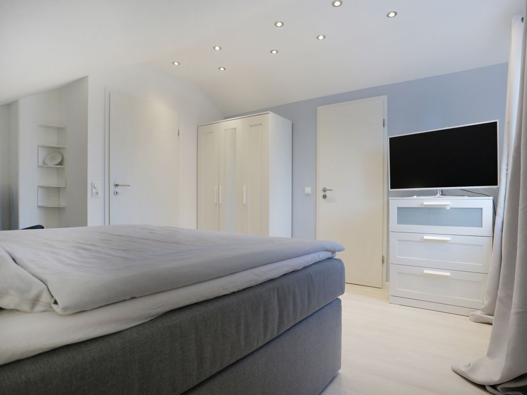 Ein modernes Schlafzimmer mit Bett, Kleiderschrank und Fernseher.