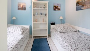 A bedroom with two single beds, a white wardrobe, and a blue rug.