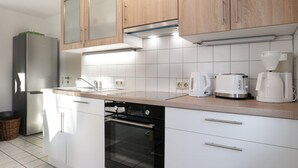 A modern kitchen with white cabinets, a stainless steel refrigerator, a built-in oven, and a coffee maker on the countertop.