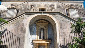 Ein historisches Gebäude mit einem zentralen Bogenportal, einer darin befindlichen Statue und einem Balkon mit Geländern.