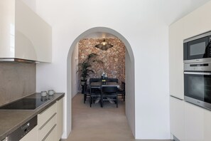 Une cuisine moderne avec une arche donnant sur un coin repas, agrémentée d’un mur en pierre et d’un luminaire suspendu.