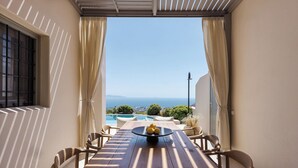 Uma varanda com mesa e cadeiras de madeira, vista para o mar e piscina ao fundo.