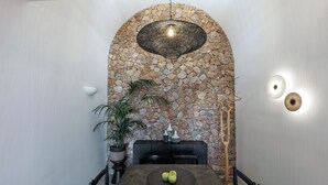 Um interior moderno com arco de parede de pedra, luminária pendente, mesa de jantar com maçãs e planta em vaso.
