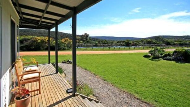 A covered outdoor area with a view of a grassy field and hills.