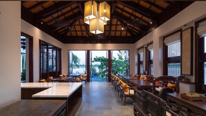 A spacious dining area with high ceilings and large windows, featuring wooden tables and chairs, and a central chandelier. - Nghe Prana Hotel and Spa Hoi An (Da Nang)