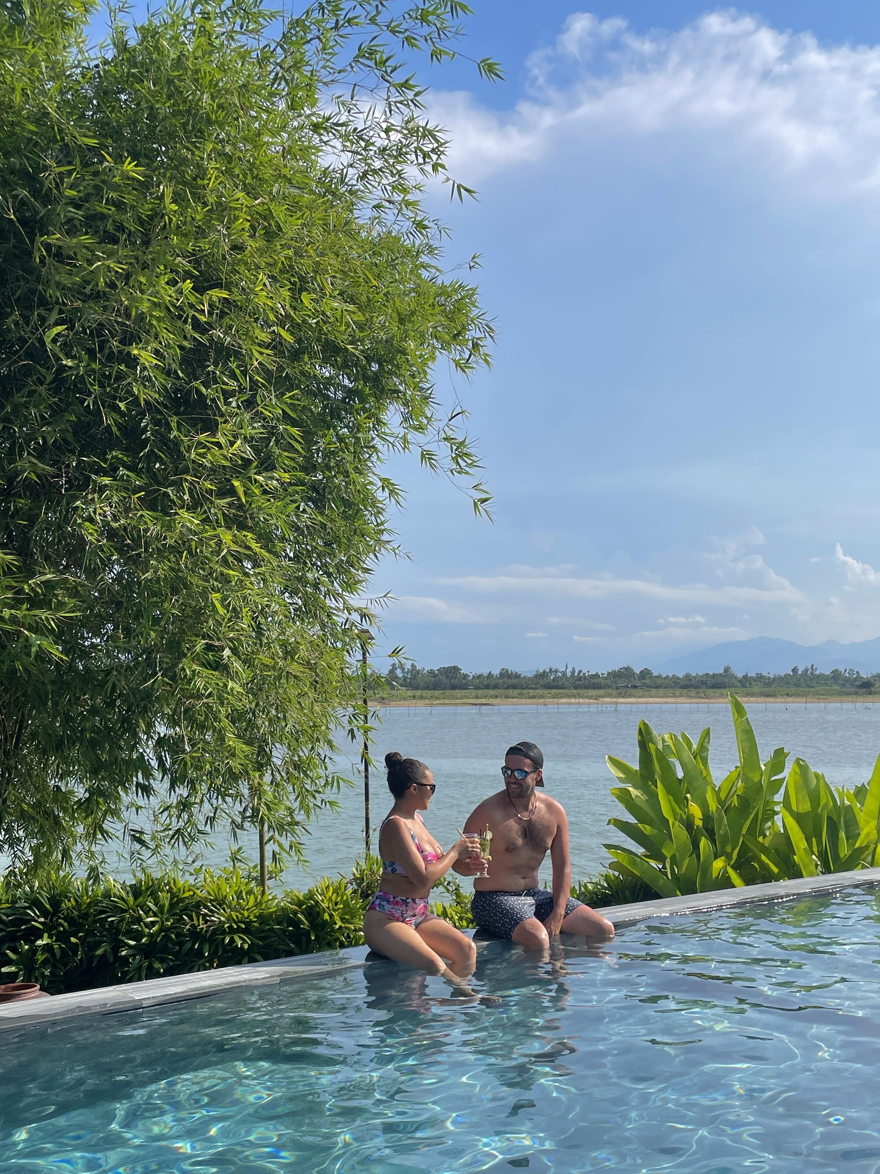 A couple sitting by a pool with a view of a lake and mountains in the background.