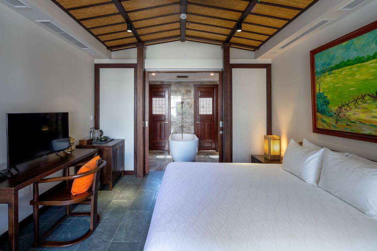 Quarto de hotel com uma cama grande, uma escrivaninha com televisão, uma banheira e um quadro na parede.