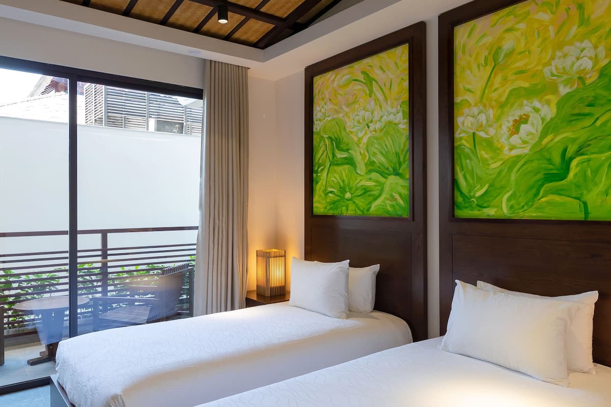 Quarto de hotel com duas camas, um ventilador de teto e grandes pinturas florais verdes nas paredes.