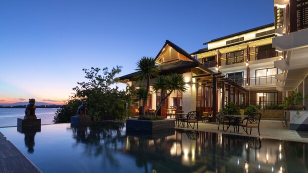 A luxurious hotel with an infinity pool, outdoor seating, and a view of the sunset over the water. - Nghe Prana Hotel and Spa Hoi An (Da Nang)