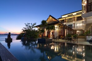 Un hotel lujoso con piscina infinita, mobiliario exterior y vistas al atardecer sobre el agua.