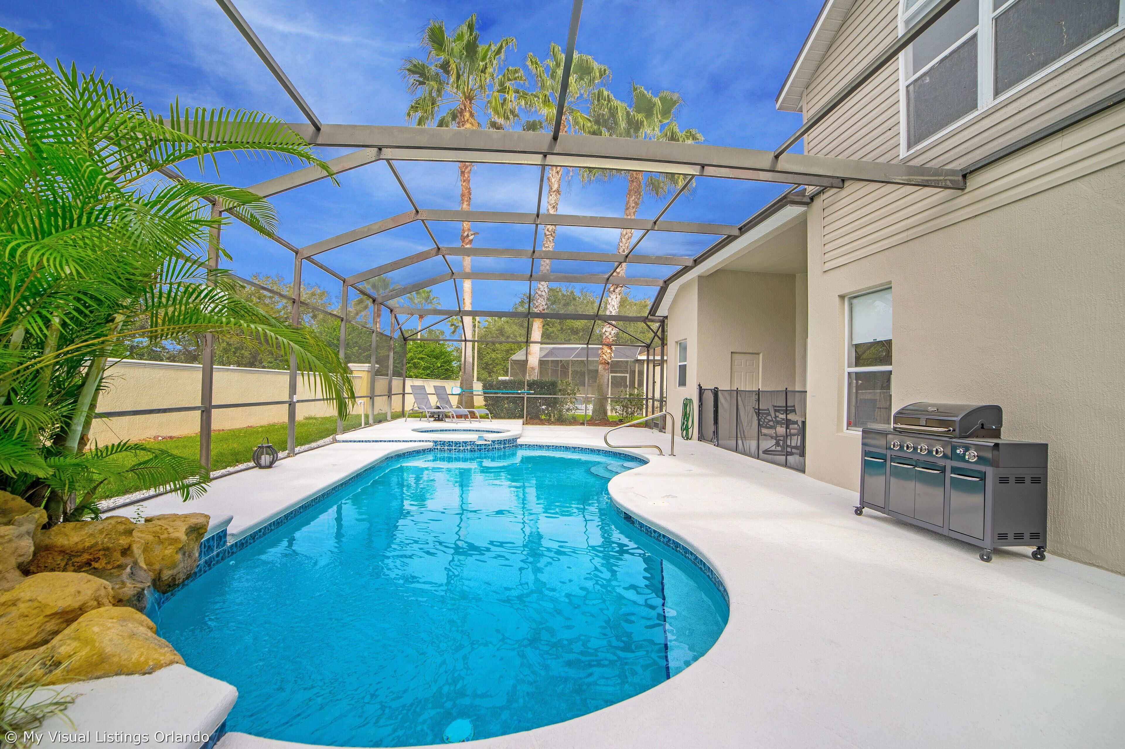 A swimming pool with a glass enclosure, a barbecue grill, and a view of palm trees.