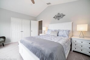 Une chambre à coucher avec un grand lit, deux tables de chevet blanches, une chaise et une armoire.