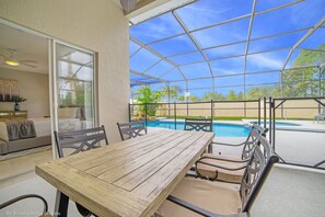 Une terrasse couverte avec une table et des chaises en bois, donnant sur une piscine.