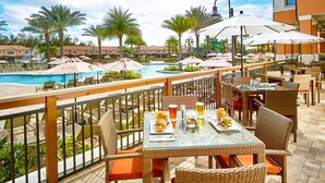 Un espace de restauration situé au bord de la piscine, avec des tables et des chaises en plein air, ainsi que des parasols, offrant une vue sur la piscine et un toboggan aquatique.