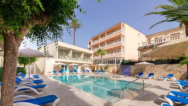 A pool area with sun loungers and umbrellas, a building with balconies, and a clear sky. - Hotel Venecia Paguera (Calvia)
