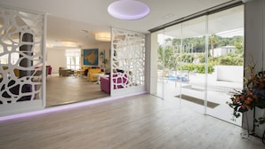 A modern hotel lobby with a wooden floor, a glass partition, and a view of the outdoors. - Hotel Venecia Paguera (Calvia)