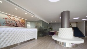 A modern lobby with a tufted reception desk, a large decorative wall, a central column, and a staircase in the background. - Hotel Venecia Paguera (Calvia)