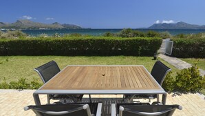 A patio with a wooden table and four chairs, overlooking a coastal landscape with mountains and the sea. - In the middle of Pollensa Bay (Apto Garrover A) (Port de Pollença)