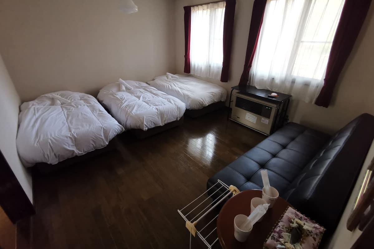 A room with two single beds, a sofa, a heater, and a small table with cups and a tissue.