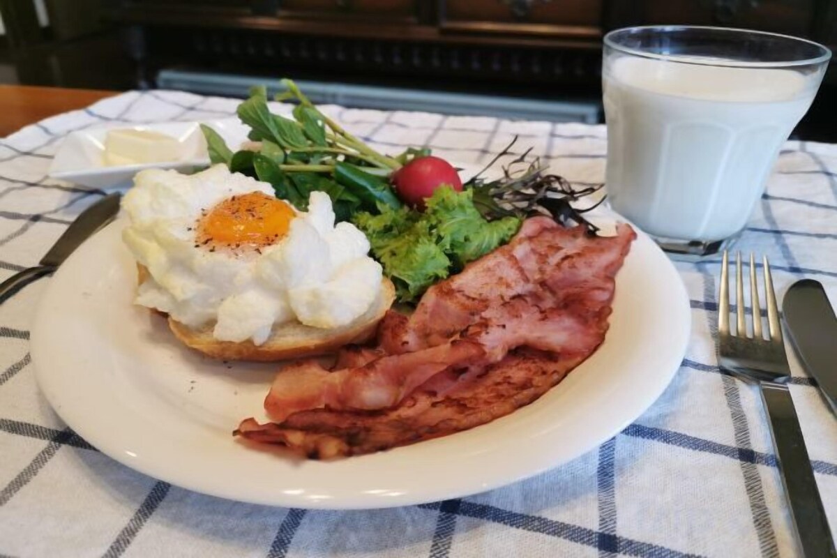 A breakfast plate with an egg, bacon, greens, and a radish on a checkered tablecloth.
