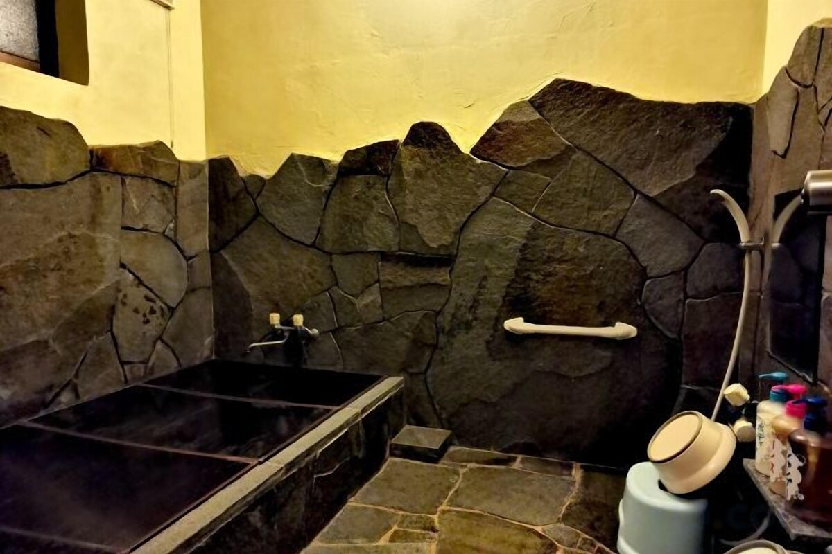 A bathroom with a stone wall, a black bathtub, and a shower area.