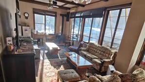 A spacious living room with a large window, a fireplace, and a ceiling fan. - Hotel Hakuba Powder Republic (Hakuba)