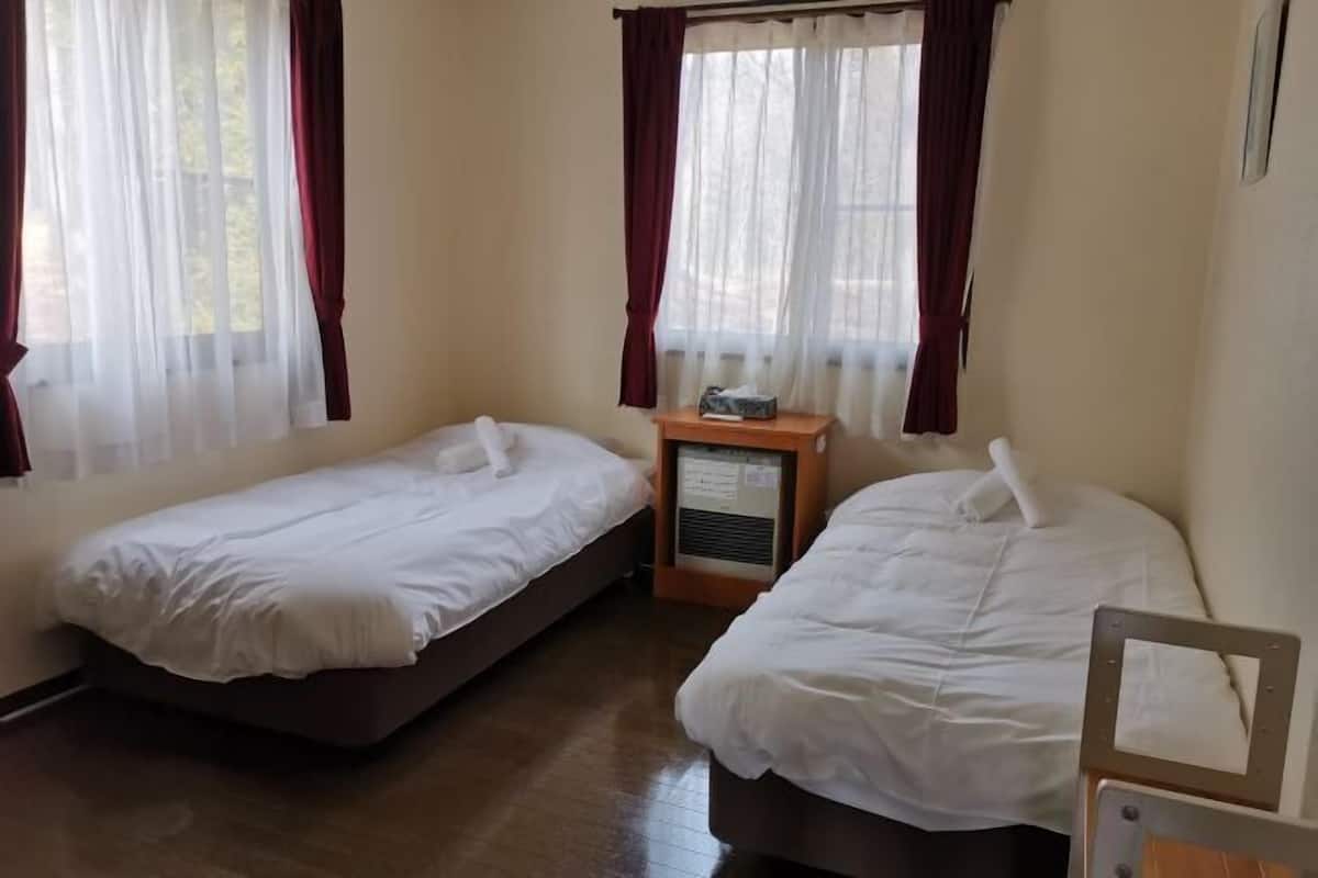 A room with two single beds, a wooden nightstand with a radio, and sheer curtains.