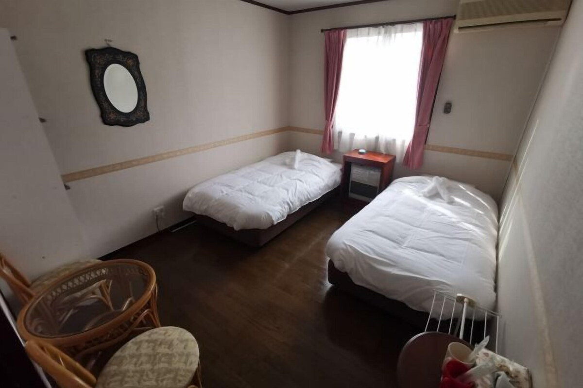 Una habitación de hotel con dos camas individuales, una mesita, una silla y un espejo en la pared.