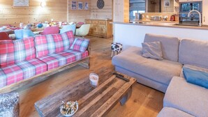 Et hyggeligt interiør med en ternet sofa, en grå sofa, et træbord og et køkken med moderne hårde hvidevarer.