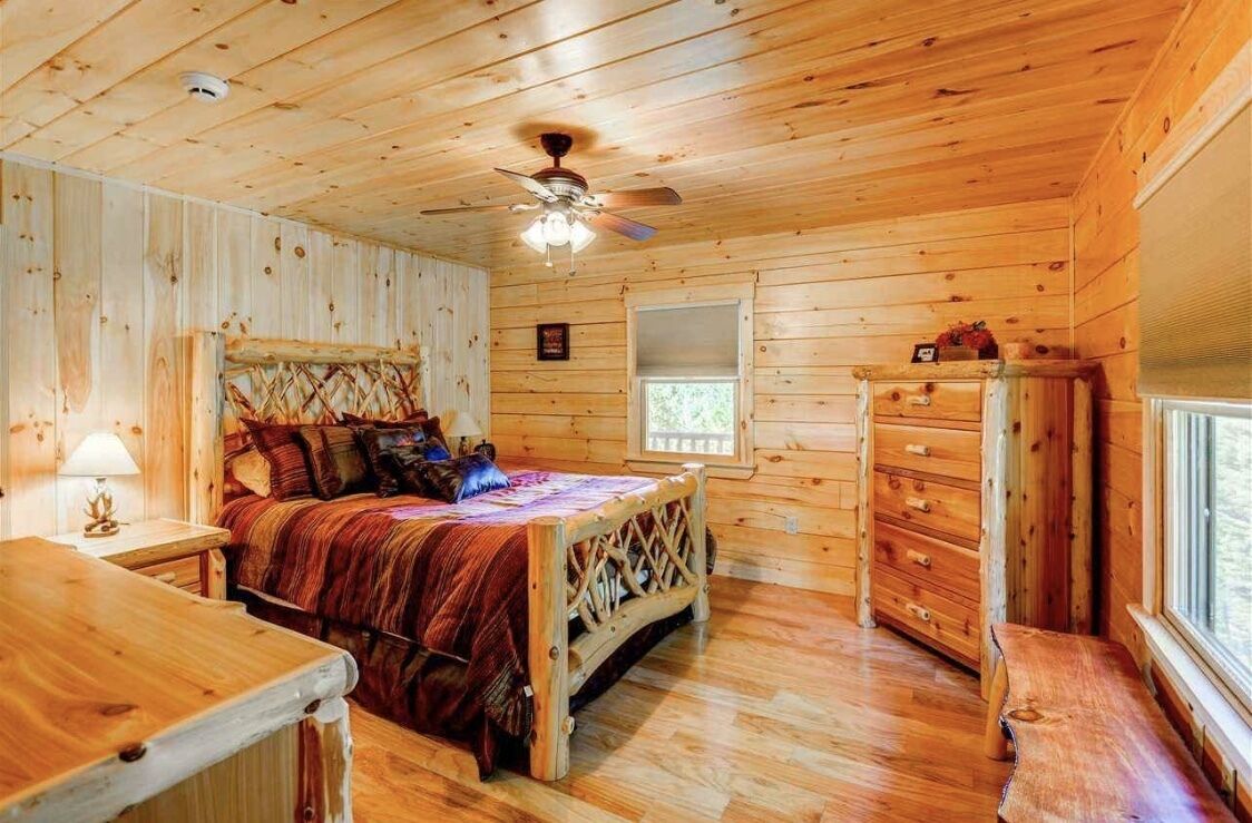 A wooden cabin bedroom with a bed, dresser, and a ceiling fan.
