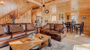 Ein geräumiges Blockhaus-Interieur mit einer Holztreppe, Ledersofas, einer Essecke und einer Küche.