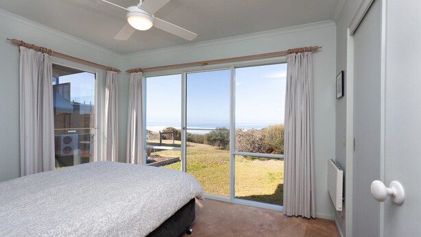 A bedroom with a bed, a ceiling fan, and a view of the outdoors.