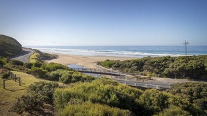 A coastal road with a beach on the right, surrounded by greenery and a clear sky.